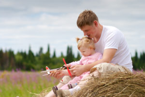 Father and daughter have fun with toy aircraft model on haystack