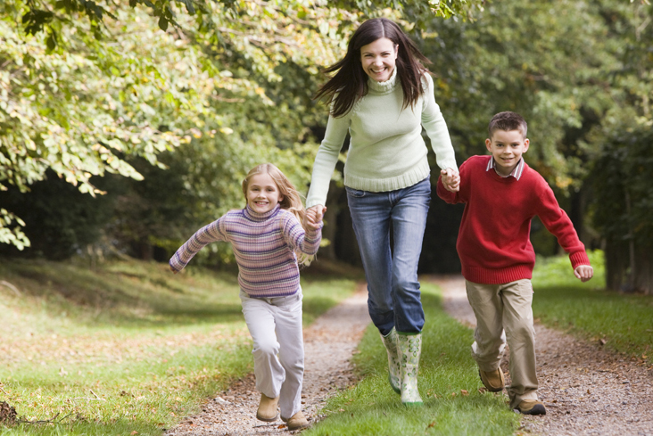 Mother and children running along woodland path in autumn